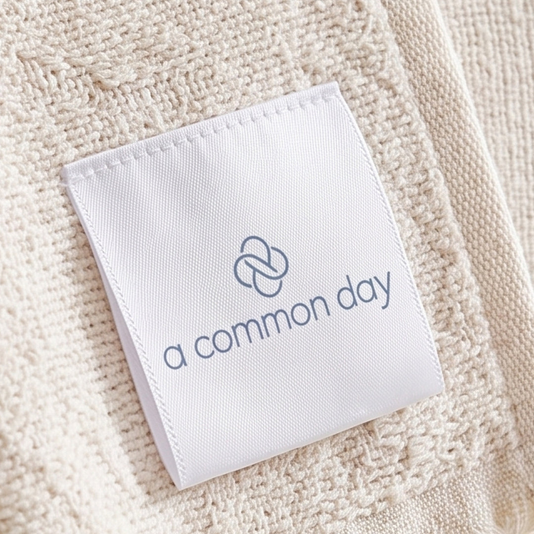 Woven A Common Day label, knot mark above the wordmark, on cream fabric