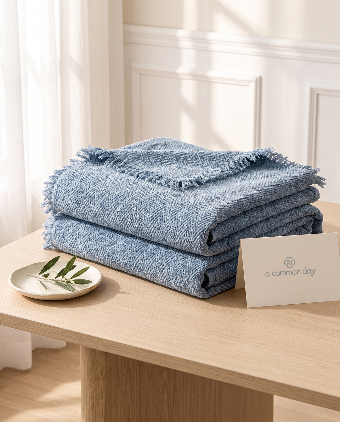 Folded blue chenille sofa covers on an oak table with an A Common Day card